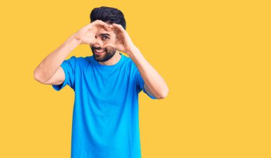 Sakallı, sıradan tişörtlü, kalp şeklinde el ve parmakları olan genç ve yakışıklı bir adam tabeladan bakıp gülümsüyor. 