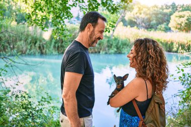 Orta yaşlı bir çift, günlük giysiler giyip parkta Chihuahua köpeği tutuyorlar.