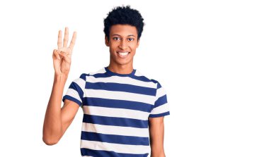 Genç Afro-Amerikalı günlük kıyafetler giymiş üç numarayı gösterip işaret ederken kendinden emin ve mutlu gülümsüyor.. 