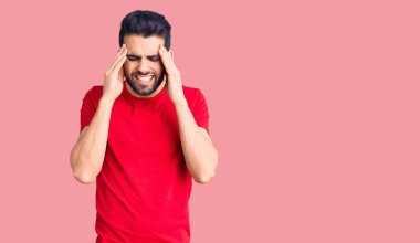 Sakallı genç yakışıklı bir adam stresten dolayı elleri başının üstünde rahat bir tişört giyiyor. migren ağrısı. 