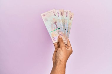 İspanyol el, izole edilmiş pembe arka planda 10 Kolombiya pezosu tutuyor..