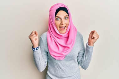 Geleneksel İslami başörtüsü takan Kafkasyalı genç bir kadın kollarını kaldırarak ve gözlerini açarak başarıyı kutluyor ve şaşırıyor. Kazanan konsept. 