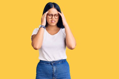 Genç, güzel Asyalı bir kız günlük kıyafetler giyiyor ve eli başının üstünde gözlük takıyor. Stres yüzünden baş ağrısı çekiyor. migren ağrısı. 