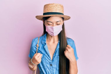 Yazın tıbbi maske takan genç Çinli kadın kolları havada ve gözleri kapalı bir şekilde başarının şaşkınlığını ve şaşkınlığını yaşıyor. 