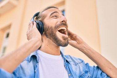 Orta Doğulu genç adam şehirde kulaklık takarak mutlu bir şekilde gülümsüyor..