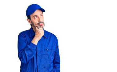 Orta yaşlı yakışıklı, elleri çenesinde tamirci üniforması giyen soru soran, düşünceli bir adam. Düşünceli bir yüzle gülümsüyor. şüphe kavramı. 