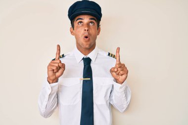 Uçak pilotu üniforması giyen genç İspanyol adam şaşırmış ve şaşırmış bir şekilde yukarı baktı ve parmaklarıyla işaret ederek kollarını kaldırdı.. 