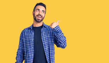 Gündelik kıyafetler giyen, gülümseyen, gülümseyen ve başparmağıyla yan tarafı gösteren İspanyol genç adam.. 