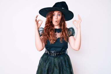 Cadı cadılar bayramı kostümü giyen genç ve güzel bir kadın şaşırmış ve şok olmuş bir şekilde parmaklarıyla onay sembolü yapıyor. çılgın ifade 