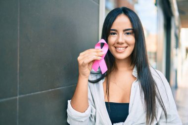 Genç İspanyol kız gülümsüyor. Şehirde pembe göğüs kanseri kurdelesi tutuyor..