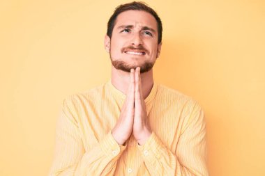 Gündelik giysiler giymiş genç yakışıklı bir adam elleri bağlı yalvarıyor ve dua ediyor. Yüzünde umut ifadesi var. Duygusal ve endişeli. Yalvarıyor. 