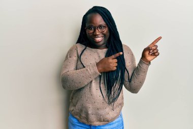 Saçları örgülü, gözlüklü, gülümseyen ve kameraya bakan iki eli ve parmağı yanda genç siyahi bir kadın.. 