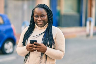 Genç Afrikalı Amerikalı kadın şehirde akıllı telefon kullanıyor..