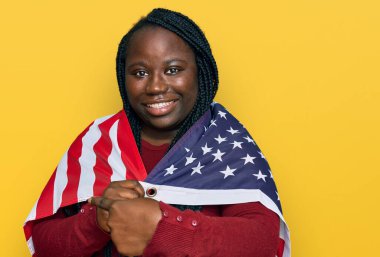 Birleşik Devletler bayrağını tutan siyah örgülü genç bir kadın mutlu bir şekilde el ve parmağıyla işaret ediyor. 