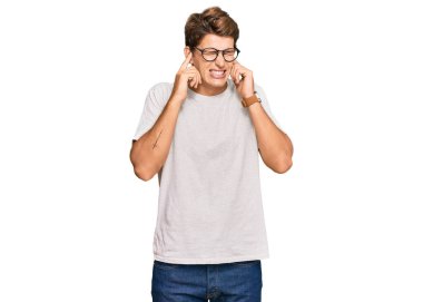 Gürültülü müzik sesi için günlük kıyafetler ve gözlük takan yakışıklı beyaz adam kulaklarını parmaklarıyla kapatıyor. sağır kavramı. 