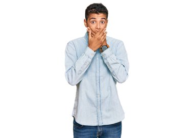 Genç, yakışıklı, Afro-Amerikalı sıradan kıyafetler giyen bir adam ağzını yanlışlıkla elleriyle kapatırken şok oldu. gizli kavram. 