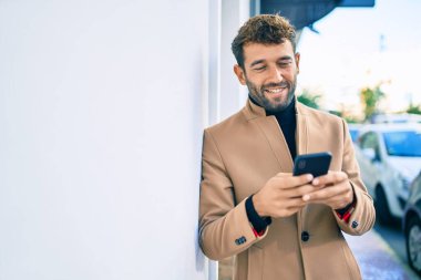 Zarif bir ceket giyen yakışıklı bir iş adamı akıllı telefon kullanarak dışarıda mutlu bir şekilde gülümsüyor.
