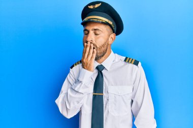 Uçak pilotu üniforması giyen sakallı yakışıklı bir adam ağzını eliyle kapatmaktan sıkılmış. Huzursuz ve uykulu.. 