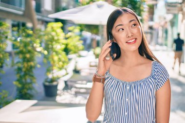 Genç Çinli kadın gülümsüyor ve şehrin caddesinde akıllı telefondan konuşuyor..