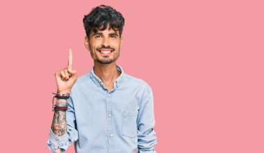 Gündelik kıyafetler giyen genç İspanyol adam başarılı bir fikirle işaret ediyor. Heyecanlı ve mutlu. Bir numara.. 