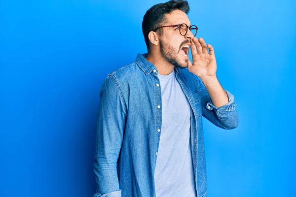 若いヒスパニック系の男がカジュアルな服や眼鏡を叫んで大声で口の上に手で横に叫んで身に着けている コミュニケーションの概念 — ストック写真