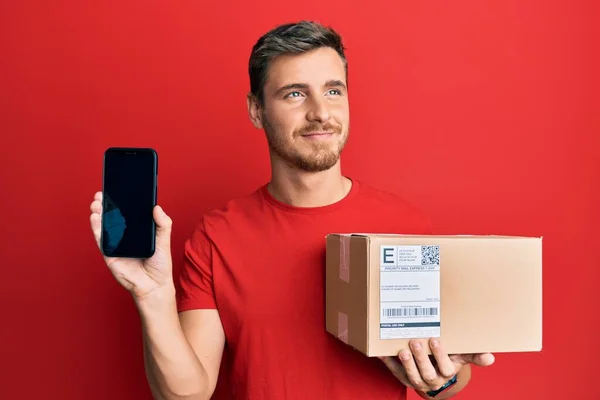 Handsome Caucasian Man Holding Delivery Package Showing Smartphone Screen Smiling — Stock Photo, Image