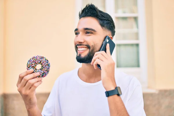 아라파 청년은 스마트폰으로 행복하게 이야기하고 도시에서 도넛을 먹으면서 — 스톡 사진