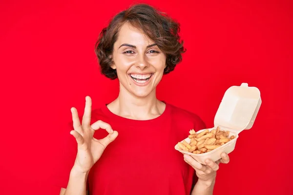 年轻的惊慌失措的女人拿着薯片 手拿着手签 微笑着表示友善的手势 是极好的象征 — 图库照片