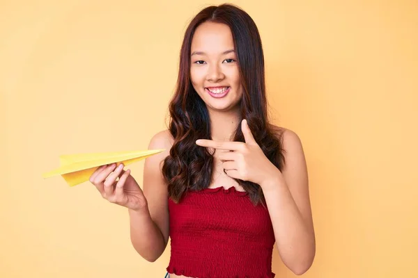 年轻美丽的中国姑娘牵着纸飞机 高兴地微笑着 手指手画脚 — 图库照片