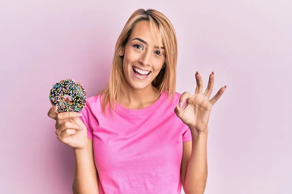 Mulher Loira Bonita Segurando Donut Fazendo Sinal Com Dedos Sorrindo — Fotografia de Stock