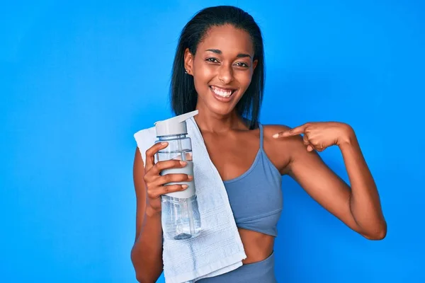 穿着运动服的年轻的非洲女人喝着一瓶水 指指点点着一个快乐而自豪的人 — 图库照片