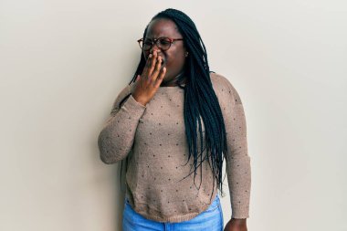 Saçları örgülü, günlük kıyafetler ve gözlükler takan genç siyahi bir kadın ağzıyla ağzını kapatmaktan sıkılmış. Huzursuz ve uykulu.. 