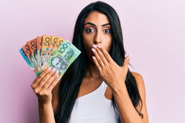 Güzel İspanyol bir kadın Avustralya dolarlarını elinde tutarak ağzını eliyle kapatıyor, şaşırmış ve hata yapmaktan korkuyor. şaşırmış ifade 