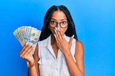 Dolarları elinde tutan güzel İspanyol bir kadın. Ağzını eliyle kapatıyor. Şok geçiriyor ve hata yapmaktan korkuyor. şaşırmış ifade 