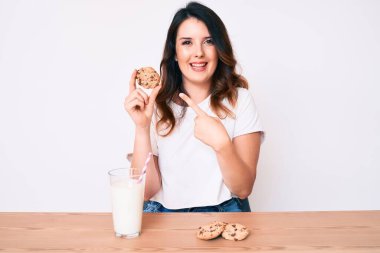 Genç, güzel esmer kadın bir bardak taze süt ve kurabiyelerle gülümsüyor. 