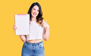 Güzel, genç, esmer bir kadın elinde boş alanı olan bir panoyla gülümseyen mutlu ve gururlu birini işaret ediyor. 