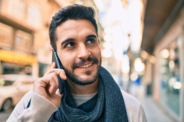 Genç İspanyol adam şehirde akıllı telefon kullanarak mutlu gülümsüyor..