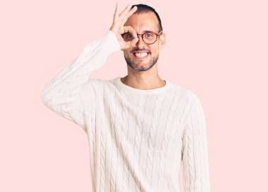 Gündelik kıyafetler ve gözlük takan genç yakışıklı adam el hareketleriyle gülümsüyor ve mutlu yüzüyle parmaklarının arasından bakıyor.. 