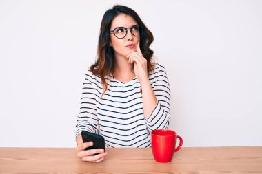 Genç, güzel, esmer bir kadın akıllı telefon kullanıyor. Ciddi bir yüz ifadesi. Soru sormayı düşünüyor. 