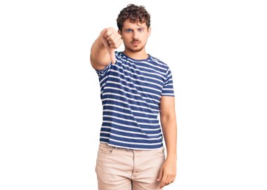 Kıvırcık saçlı, sıradan giyinen, mutsuz görünen, reddedilmiş ve olumsuz davranan genç yakışıklı bir adam. kötü ifade. 