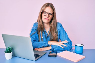 Ofiste çalışan genç sarışın kız şüpheci ve gergin bir fincan kahve içiyor ve kollarını kavuşturup yüz ifadesini onaylamıyor. negatif kişi. 