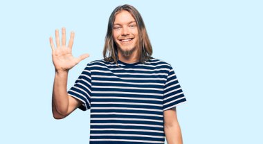 Uzun saçlı yakışıklı beyaz adam. Sıradan çizgili tişört giyiyor. Beş numarayı gösteriyor ve gülümsüyor.. 