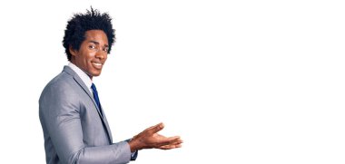 Handsome african american man with afro hair wearing business jacket pointing aside with hands open palms showing copy space, presenting advertisement smiling excited happy 