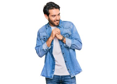 Gündelik kıyafetler giyen genç İspanyol adam gergin ve heyecanlı, elleri çenesinde yan tarafa bakıyor. 