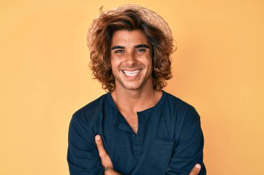 Yazlık şapkalı, mutlu yüzlü, kollarını kavuşturup kameraya bakan İspanyol bir genç. pozitif kişi. 