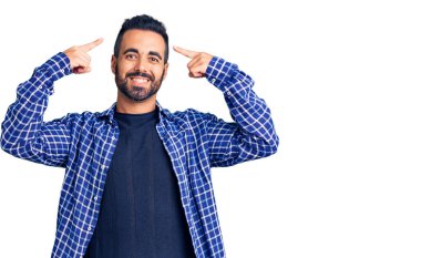 Gündelik kıyafetler giyen genç İspanyol adam gülümseyerek iki eliyle kafasını işaret ediyor. Harika bir fikir ya da düşünce, iyi bir hafıza. 