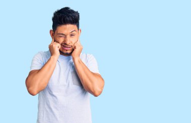 Yakışıklı Latin Amerikalı genç adam, gündelik kıyafetler giyip yüksek sesli müzik sesi için kulaklarını parmaklarıyla kapatıyor. sağır kavramı. 