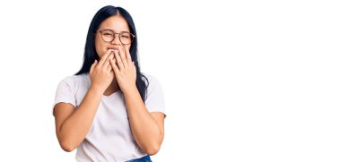 Genç ve güzel Asyalı kız günlük kıyafetler ve gözlük takıp gülüyor ve utanıyor kıkırdıyor ağzı ellerle, dedikoduyla ve skandal konseptiyle örtüyor. 