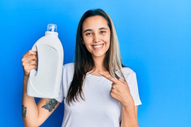 Genç İspanyol kadın elinde deterjan şişesi tutuyor. Korkmuş ve ağzı açık kalmış, şaşırmış ve şaşırmış. 