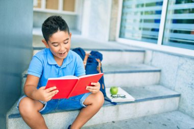 Okulun merdivenlerinde kitap okuyan sevimli öğrenci çocuk..